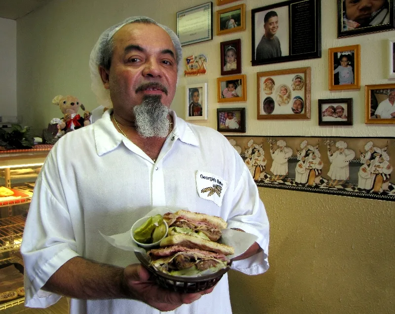 George Ruiz in the bakery, holding a Cuban sandwich